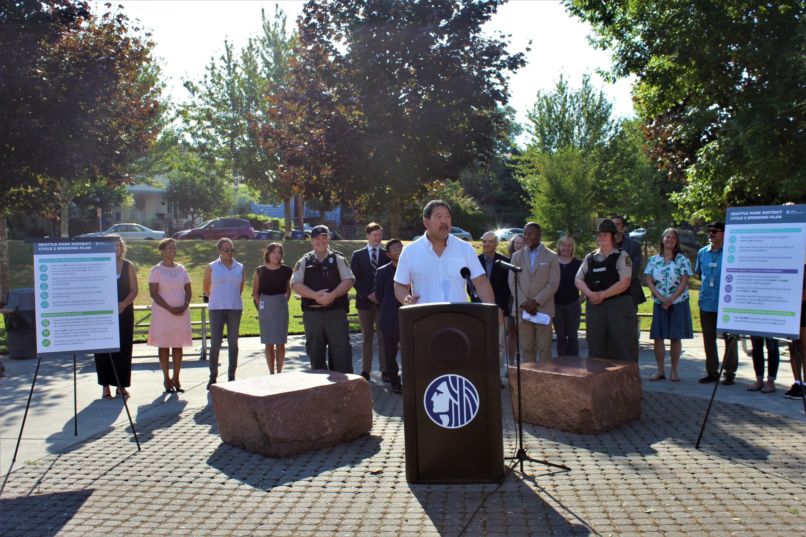 Mayor Harrell stands behind a podium at Rainier Playfield with a staff behind him.
