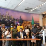 Mayor Harrell signs cannabis equity legislation while stakeholders stand behind him.
