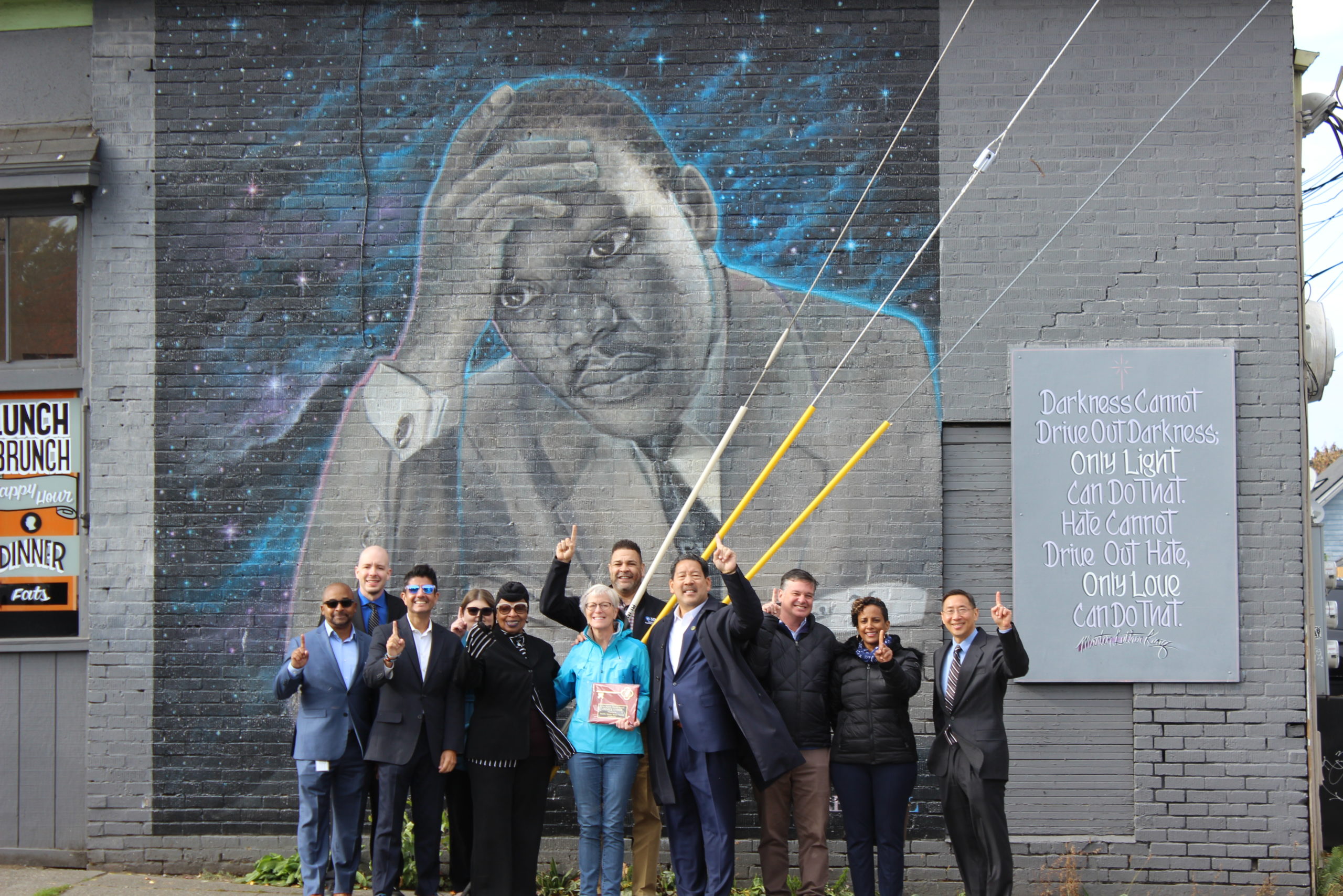 Mayor Harrell and team pose in front of MLK Jr. mural and hold up index finger for "One Seattle"