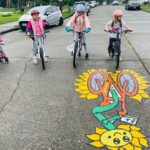 Seattle kids riding bikes on their way to school, street mural of sunflower on a bicycle