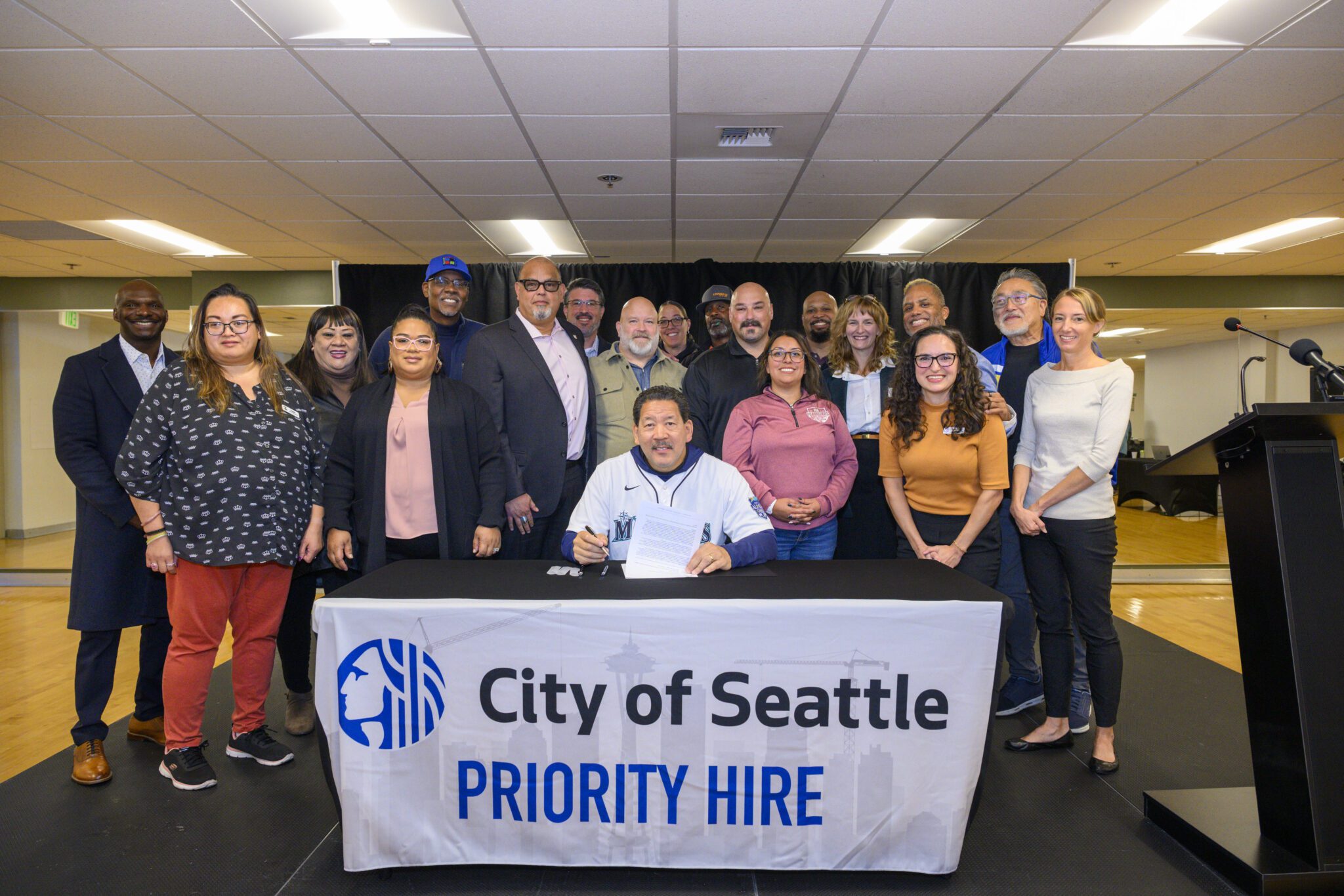 Mayor Harrell signs the directive with labor and community partners behind him.
